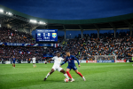 French player dribbling soccer ball past Ivorian defender in stadium with scoreboard showing France 1 Côte d'Ivoire 0